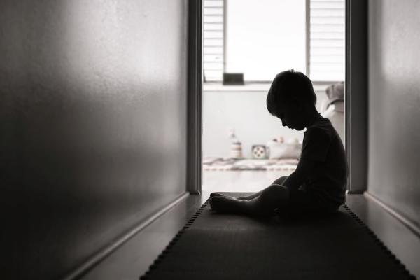The image displays a sad child in a hallway