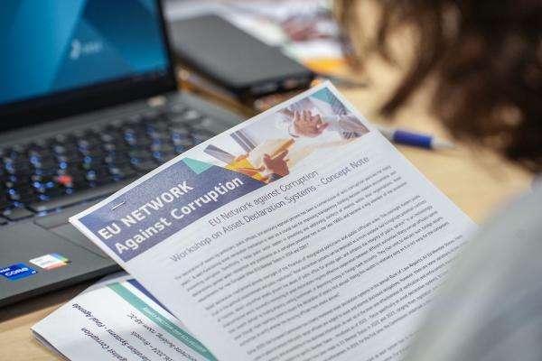 Photo from the workshop showing a person reading a document, titled "EU network against corruption".
